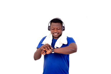 Spor kıyafetli genç adam beyaz arka planda durup saatine bakarken kulaklıkla müzik dinlerken gülümsüyor..