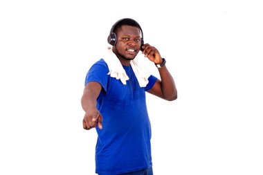 Spor kıyafetli genç adam beyaz arka planda durup kulaklıkla müzik dinlerken parmağıyla gülümsüyor..