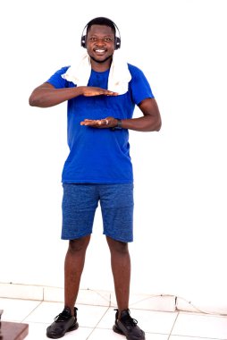 Spor kıyafetli genç adam spor salonunda, kulaklıkları ve boynunda havluyla gülümserken belinin ince olduğunu gösteriyor..