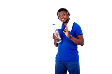 Boynunda havluyla, kulaklık takan, plastik su şişesi tutan ve parmaklarıyla gülümseyerek hareket eden genç sporcu..