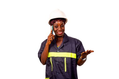 Güzel bir kadın mühendisin portresi beyaz başlık takıyor ve iş üniforması giyiyor cep telefonuyla konuşuyor ve gülümserken el hareketi yapıyor..