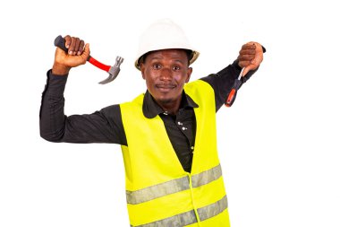 Yeşil yelek ve kasklı genç bir teknisyen elinde çekiç ve gülümseyen bir tornavida tutuyor..