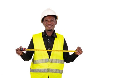 Genç marangoz yeşil yelek giyiyor ve elinde mezura tutarken gülümsüyor..