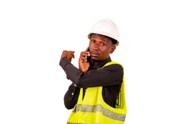 Güvenlik kasklı bir inşaat mühendisi beyaz arka planda duruyor ve cep telefonuyla yön gösteriyor..
