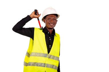 Genç mühendis yeşil yelek giyiyor ve elinde çekiç tutarken gülümsüyor..