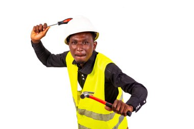 Yeşil yelek ve kasklı genç bir teknisyen elinde çekiç ve gülümseyen bir tornavida tutuyor..