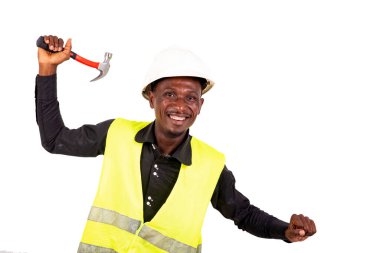 Genç teknisyen yeşil yelek ve güvenlik kaskı takıyor ve elinde çekiç tutarken gülümsüyor..