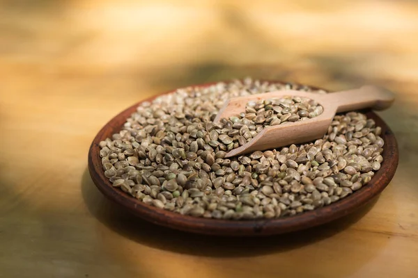 Hemp seeds in a clay dish. Wood background.