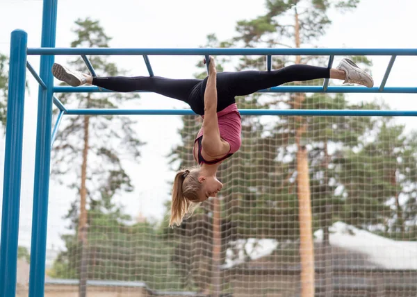 Pasująca blondynka atrakcyjna kobieta robi split wiszące do góry nogami w strefie sportowej na świeżym powietrzu w lecie, selektywne skupienie. — Zdjęcie stockowe