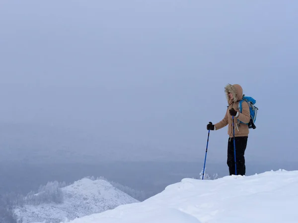 Caminhante em outerwear quente com mochila e bastões de esqui andando sobre a neve nas montanhas no inverno, céu nebuloso, foco seletivo. — Fotografia de Stock