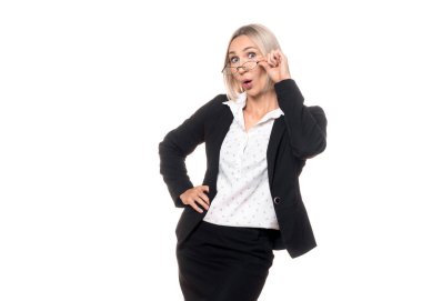 Şaşkın iş kadını. Resmi giyinmiş yetişkin bir beyaz kadın, beyaz arka planda izole edilmiş, merak dolu bir yüz ifadesiyle gözlüklerine bakıyor..