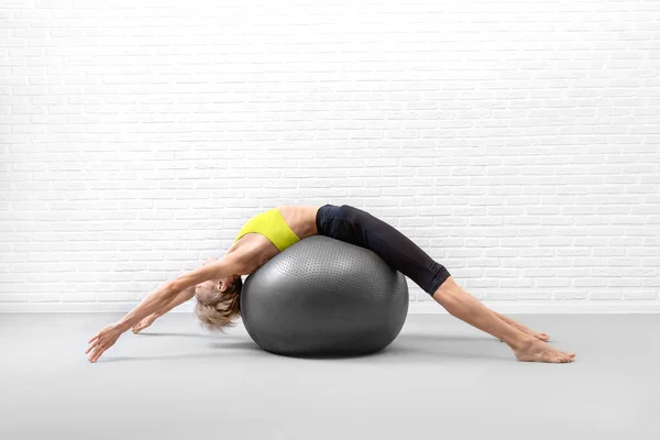 Спина растягивается с фитнес-мяч. Тонкая белая женщина лежит на большом шаре для упражнений и растягивает позвоночник в помещении студии на чердаке.. — стоковое фото