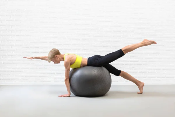Класс пилатеса с мячом. Тонкая привлекательная белая женщина практикует балансировку в помещении студии. — стоковое фото