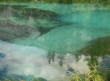 Gölün sakin, pürüzsüz yüzeyinde ağaçların ve bulutların güzel yansıması.