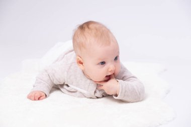 Sevimli bebek yerde yatıyor ve küçük parmaklarını emiyor, beyaz arka plan 