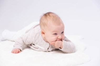 Sevimli bebek yerde yatıyor ve küçük parmaklarını emiyor, beyaz arka plan 
