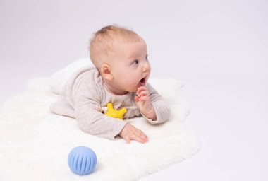 Yerde beyaz arka planda bir oyuncakla oynayan güzel bir bebek.