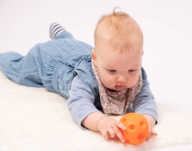 Çekici bebek turuncu bir topla oynuyor, beyaz arka planda.