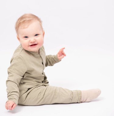 Çekici bebek beyaz zeminde oturuyor ve gülümsüyor.