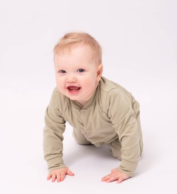 Çekici bebek beyaz zeminde oturuyor ve gülümsüyor.