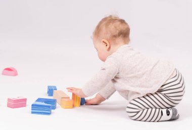 Çekici bebek beyaz zeminde oyuncaklarla oynuyor.