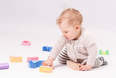 Çekici bebek beyaz zeminde oyuncaklarla oynuyor.