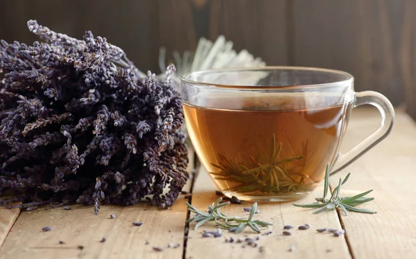Lavender herbal leaf tea in a glass cup with lavender bouquet and herb leaves nearby on rustic wooden table, closeup, copy space, herbal drinks and naturopathy concept