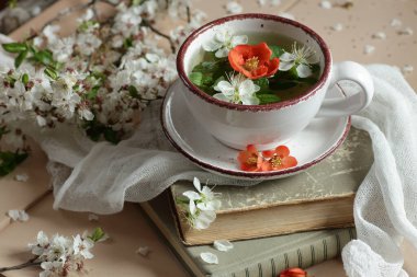 Bahar çiçekli nane çayı, çiçek tomurcukları elma ağacı ve bıldırcın çiçeği çiçekleri, antika retro kompozisyon ve kitaplarla ve çiçek açan dallarla yaşam, yakın plan, kopyalama alanı, paskalya ve bahar çiçekli içecekler konsepti