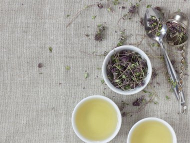 Kekik kurutulmuş çiçek çayı keten tekstil üzerinde yakın çiçekli ve kaşıklı beyaz bardakta, yakın plan, kopyalama alanı, düz alan, yukarıdan bakıldığında, sağlıklı bitkisel çaylar ve doğal destek konsepti