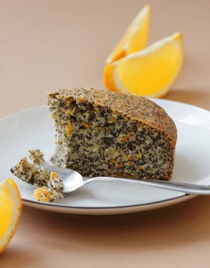 Haşhaş tohumu ve portakal kabuğu vejetaryen yumurtasız ve sütsüz kek, yanında mavi keten tekstil ve haşhaş kafası olan turuncu tabağı ısır, yakın plan, kopyalama alanı, vejetaryen yemeği ve hamur işi kavramı