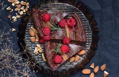 Chocolate vegan brownie cake with banana decorated with raspberry, walnut and rosemary, closeup, copy space, vegan eggfree desserts concept clipart