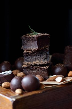 Çikolatalı brovniler, badem, koyu siyah karamsar arka planda biberiye ile süslenmiş kakao tozu, fotokopi alanı, dikey, vegan yumurtasız ve glütensiz tatlı konsepti.