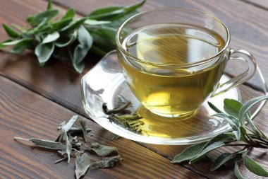 Kırsal ahşap arka planda taze ve kurumuş yapraklarla dolu bir bardak içinde adaçayı, yakın plan, kopyalama alanı, doğal tıp ve sağlıklı homeopatik bitkiler konsepti.