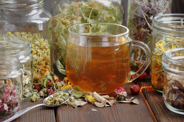 Herbal tea and jars with dry homeopathic herbs: chamomile, linden, calendula, burdock, rosehips and flowers, closeup, copy space, naturopathy and natural medicine concept