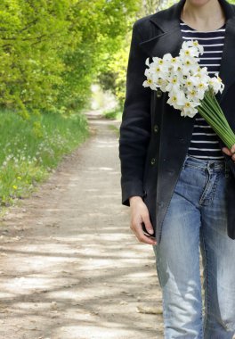 Sıradan giyinmiş bir kadın bir buket nergis, mahsul, yakın çekim, fotokopi alanı, vahşi yaşam tarzıyla bağlantı ile vahşi doğada yürüyor.