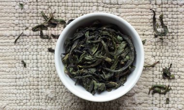 Rosebay Willowhere, beyaz bir kasede, örülmüş gri pamuk kumaş, yakın plan, geleneksel Rus içeceği, doğal bitki çayları, naturopati ve yeşil tıp konsepti üzerine mayalanmış yeşil çay.