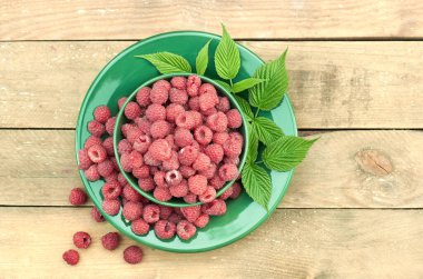 Taze yapraklar ve meyvelerle dolu bir kasede ahududu, ahşap masaya saçılmış, yakın plan, fotokopi alanı, sağlıklı vegan yeme ve organik ev yapımı gıda konsepti.