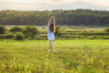 Genç ve güzel bir kadın vahşi doğaya doğru koşuşturuyor: çayır, göl ve orman, mavi elbiseli kadın geriye bakıyor ve gülümsüyor, kopyalama alanı, yaşam tarzı, doğa kavramı ile bağlantı