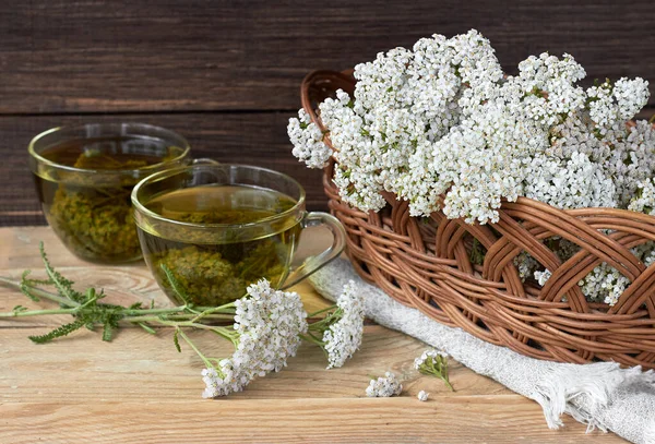 Yarrow herbal healing tea or decoction with fresh milfoil flowers nearby on rustic table on wooden background, closeup, copy space, alternative medicinal and naturopathy concept