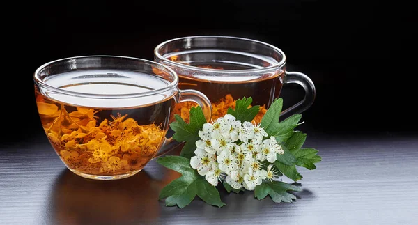 Haw herbal healing flower tea from hawthorn bloom with blossom of  a tree nearby on wooden table isolated on black background, closeup, copy space, cardiovascular disease herbs concept