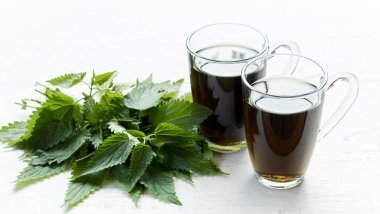 Cam fincanlarda ısırgan otu çayı ve beyaz ahşap masada izole edilmiş taze urtica otu, Urtica dioica polivitaminik bir beslenme gıdası ve kozmetik malzeme, yakın plan, boş alanı kopyalama, şifalı bitki konsepti