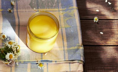 Eritilmiş tereyağlı ghee cam kutunun içinde, ahşap masanın yanında papatya çayı bulunan pembe tekstil üzerinde, ayurvedic tedaviyi iyileştiriyor ve günlük yemek, düz yatak, üst manzara, yakın çekim için çok lezzetli bir ürün.