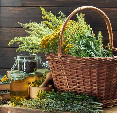 Herbal helminthic triad: absinth, tansy and cloves; fresh herbs in the wicker basket and wooden mortar, on old books,  healing infusion is nearby, closeup, copy space, antihelminthic medicine concept clipart