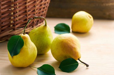 Ahşap sepetin önündeki ahşap masanın üzerine pembe armutlar serilmiş taze taze bahçe sarısı, ahşap arka planda bir armut kaybolmuş, tasarımın için kopyalama alanı, yakın plan.