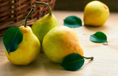 Yeşil yapraklı sarı armutlar ahşap sepetin önündeki ahşap sepetin üzerine serilmiş. Bir armut, ahşap arka planda kaybolmuş, boşluğu kopyala