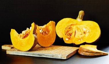 Tahta kesim tahtasında taze balkabağı parçaları, koyu siyah arka planda sağlıklı sebze yemekleri, yakın plan, fotokopi alanı, doğal organik vitamin besin konsepti.