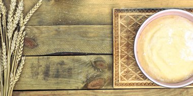 Pembe bir kasede hamur işi, sağda buğday filizi demeti var. Kabataslak kaba ahşap zemin üzerinde. Tasarımınız için merkezde boş alan var.