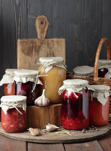 Variety of canned vegetable food: conserved beetroot, tomato paste, preserved bean, jam, pickles on wooden rustic background, canned produce, saving leftovers, home food storage organization concept