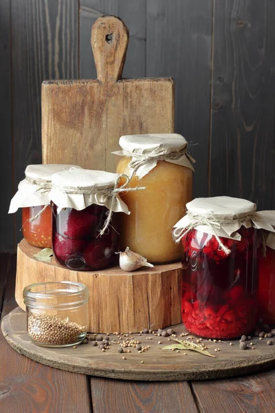 Variety of canned vegetable food: conserved beetroot, tomato paste, preserved bean, jam, pickles on wooden rustic background, canned produce, saving leftovers, home food storage organization concept