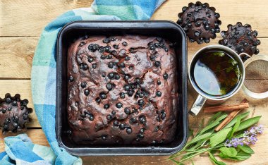 Kek ve otlu çikolatalı yaban mersinli pasta: yakınlarda nane, lavanta, adaçayı ve tarçın ve kırsal ahşap masa üzerinde bir fincan kekik çayı, düz konum, yukarıdan bakıldığında, yakın plan, kopyalama alanı, ev yapımı yumurtasız tatlı konsepti